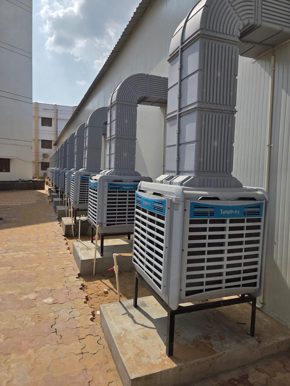 Ground-mounted industrial air coolers feeding cooled air into a warehouse through GI ducts.